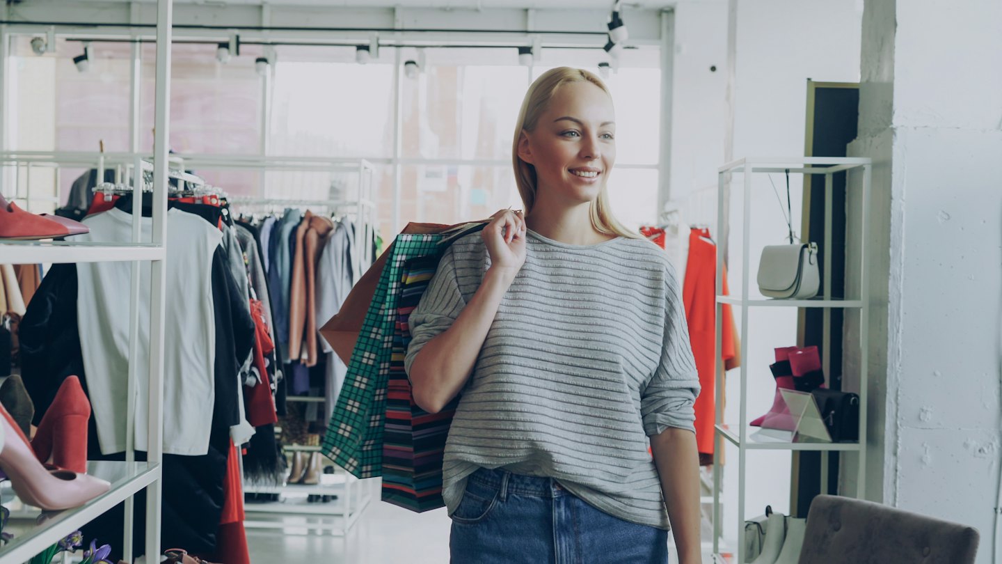 Woman smiles carrying shopping bags in a clothing boutique.