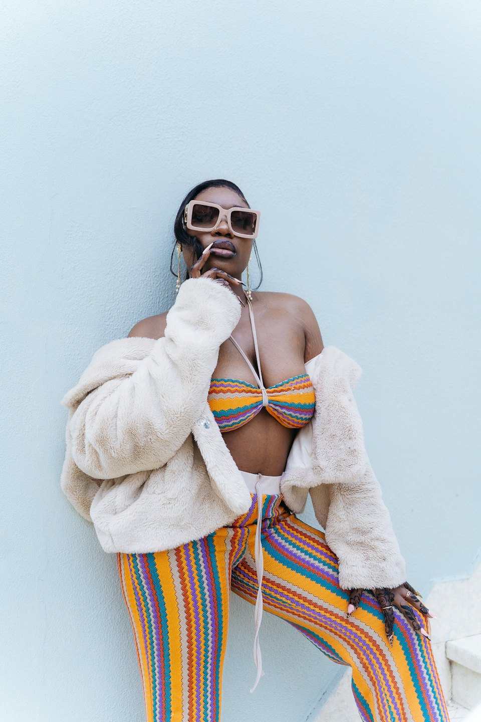 Woman in a striped outfit and faux fur jacket poses.