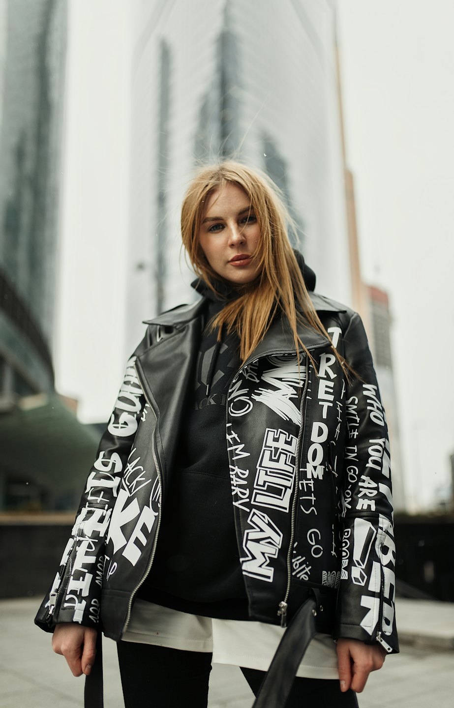 Woman in graffiti jacket with modern buildings behind her.